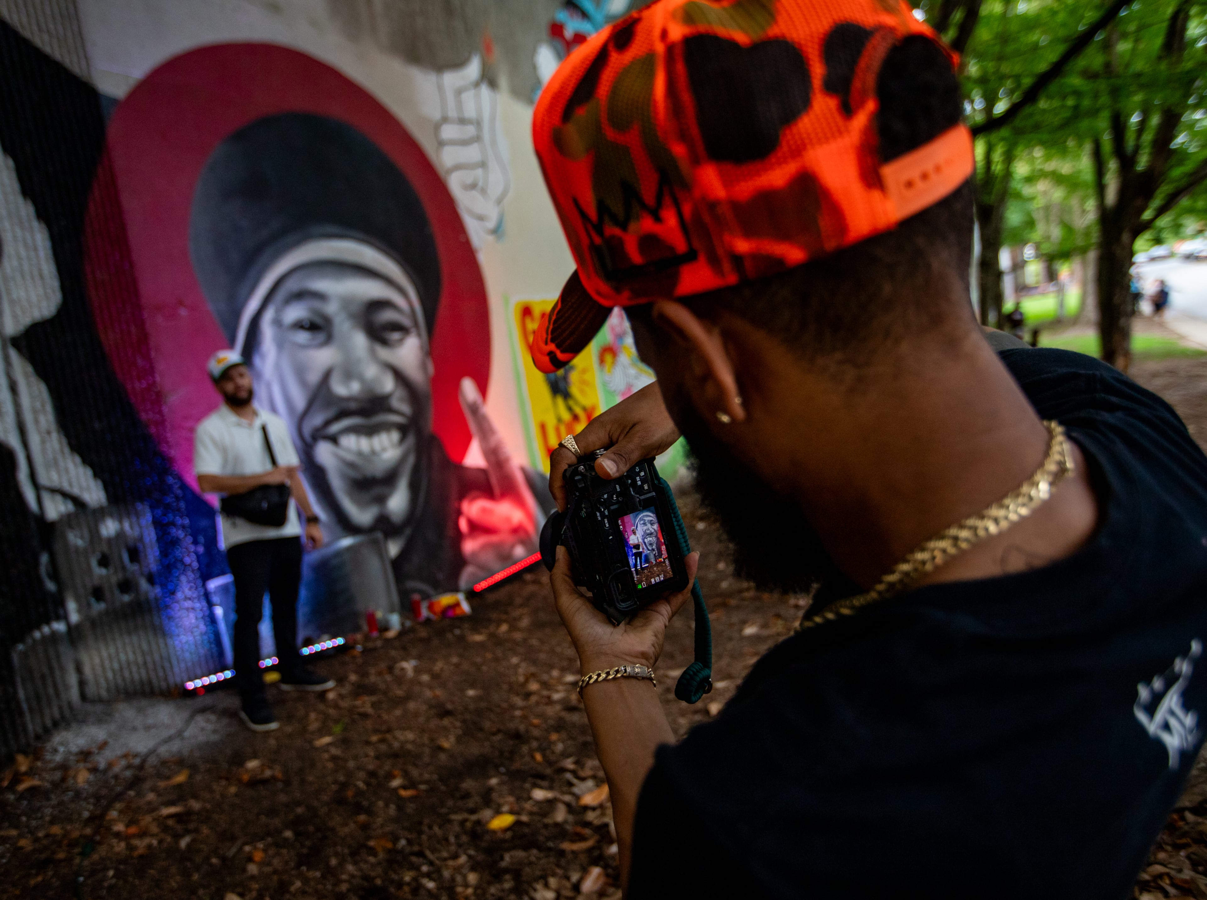 Family, friends and creatives gather to remember Andre "D.R.E.S. Tha Beatnik" Lett at a vigil on Friday, June 13, 2025, in Cabbagetown. D.R.E.S.' brother King Shands takes photos at the mural with Brick DuBose before the formal program begins. (Jenni Girtman for the AJC)