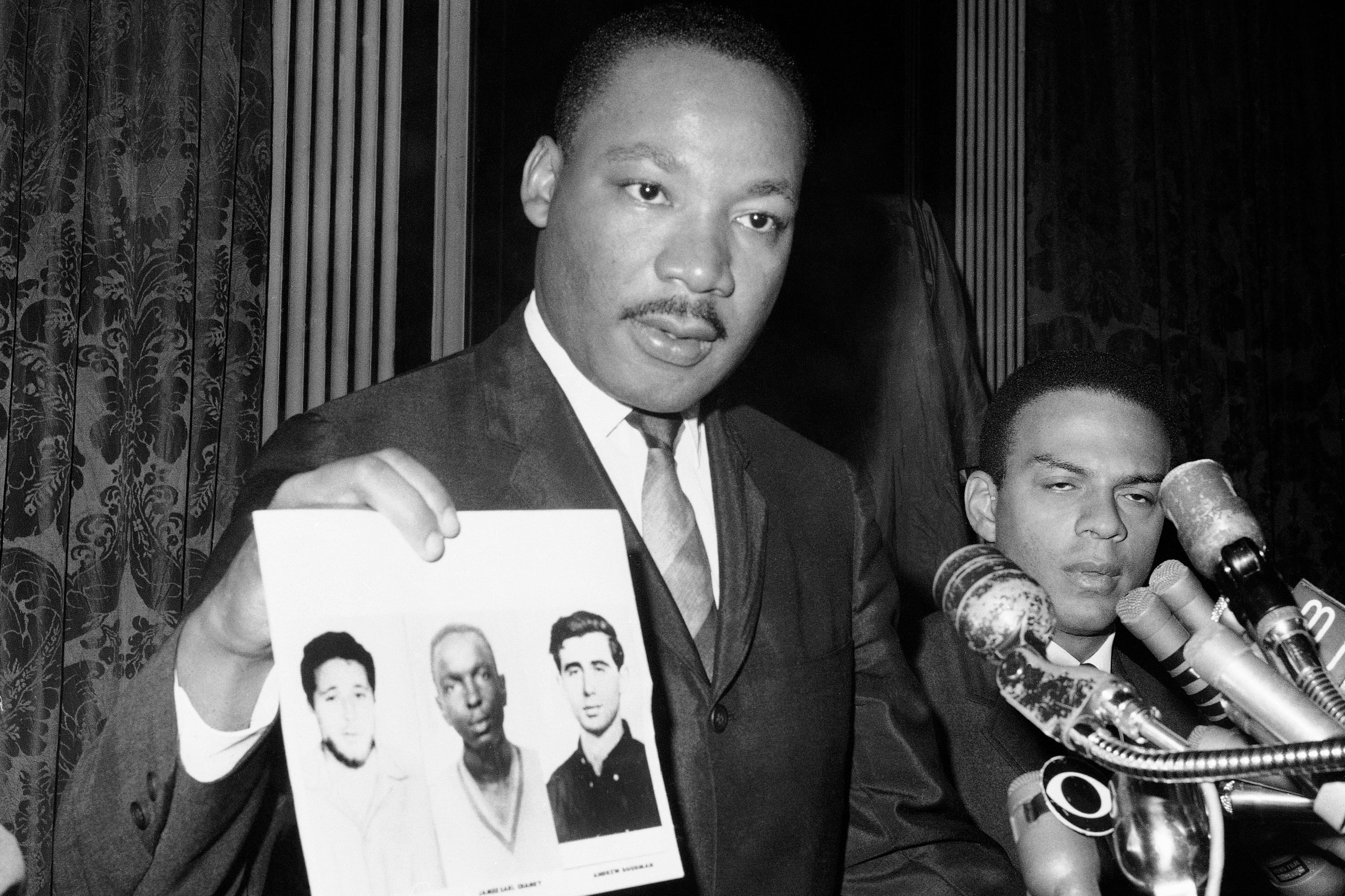 Civil rights leader Martin Luther King Jr. displays pictures of three civil rights workers, who were slain in Mississippi the summer before, from left Michael Schwerner, James Chaney, and Andrew Goodman, at a news conference on Dec. 4, 1964, in New York, where he commended the FBI for its arrests in Mississippi in connection with the slayings. (JL/AP)